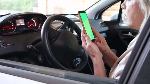 一位年事已高 驾驶汽车的老年妇女在绿色屏幕上使用智能设备 — 图库视频影像