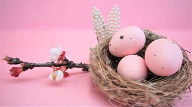 Paskalya kompozisyonu yumurta ve pembe pastel arka planda küçük incilerden yapılmış tavşan kulakları. Bir dal çiçek açan sakura.