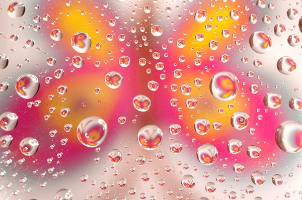 Vattendroppar som små linser över en färgad bakgrund. — Stockfoto