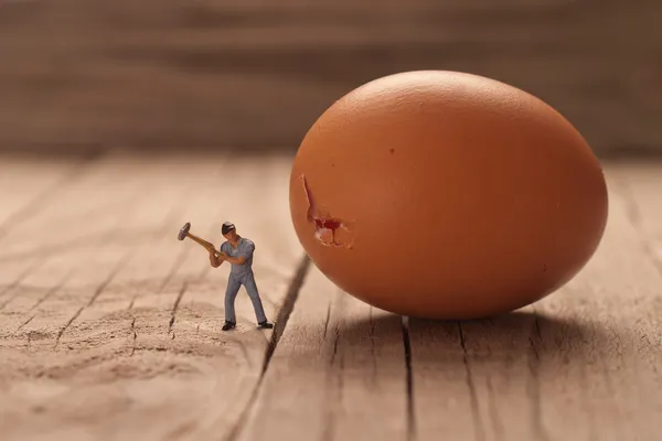 Маленький человек разбивает яйцо. Концепция приготовления пищи — стоковое фото