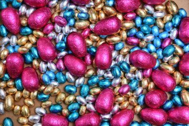 Küçük pembe, mavi, gümüş ve altın folyo sarıp sarmalanmış, büyük pembe yumurtaları soluk ahşap arka planda.. 