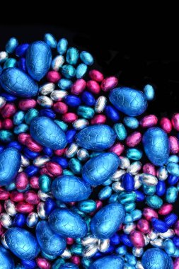 Büyük ve küçük pembe, mavi ve gümüş folyo kaplanmış paskalya yumurtaları, siyah bir zemin üzerinde. 