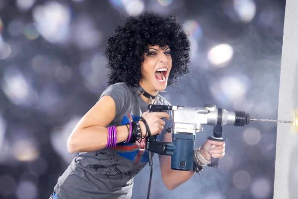 Curly brunette met een elektrische boor op lichte achtergrond — Stockfoto