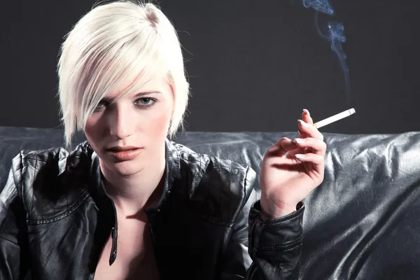 Fille blonde fumant une cigarette sur un canapé noir — Photo