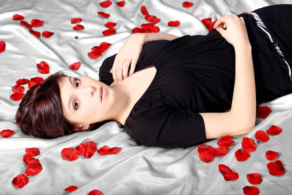 Brunette meisje liggend op een bed van rozen — Stockfoto