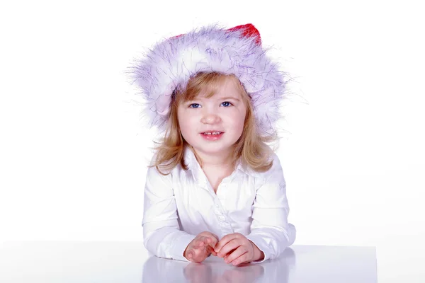 一个戴着圣诞帽的年轻女孩坐在桌旁 — 图库照片