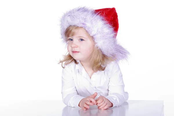 A young girl in a Christmas hat sits at the table — Stock Photo, Image