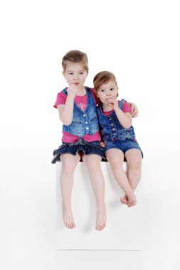 Beyaz bir podyum üzerinde oturan iki küçük kız