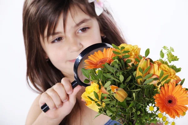 Little girl looking through a magnifying glass on a bouquet of flowers — Stock Photo, Image