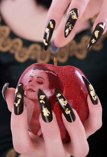 A girl with long nails holding an apple with a display of a woman's face — Stock Photo, Image