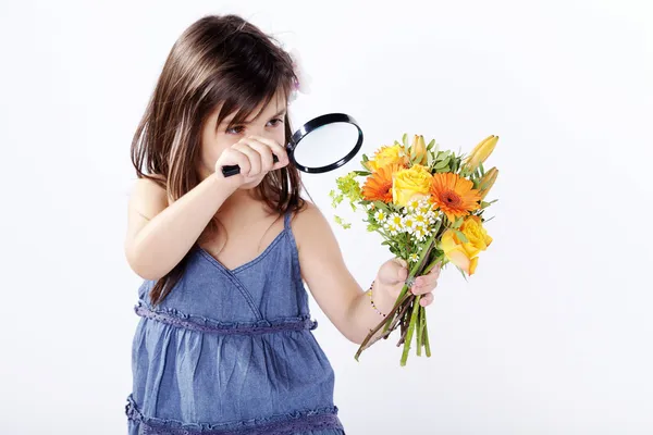 Little girl looking through a magnifying glass on a bouquet of flowers — Stock Photo, Image