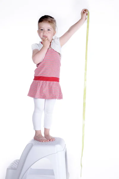 Liten flicka står på en stol och det mäter din längd — Stockfoto