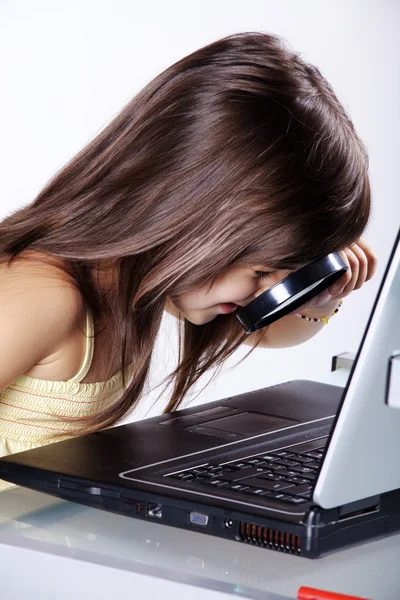 Meisje kijkend door een vergrootglas op een laptop — Stockfoto