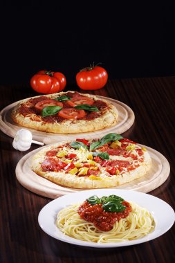two pizzas, pasta and tomato on a wooden table clipart