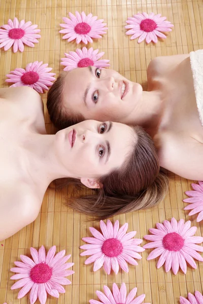 Δύο μελαχρινή κοπέλα ξαπλωμένος σε ένα ξύλινο χαλί με ροζ λουλούδια — Φωτογραφία Αρχείου