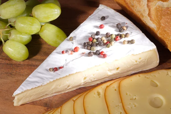 Cheese, cake and grapes on a wooden board — Stock Photo, Image