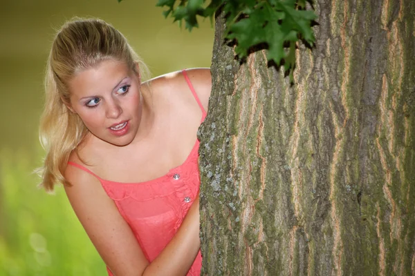 Blond meisje gluren achter een boom — Stockfoto
