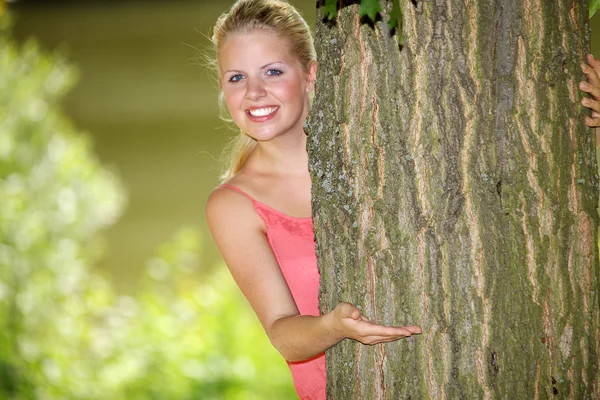 Blonde girl peeking from behind a tree — Stock Photo, Image