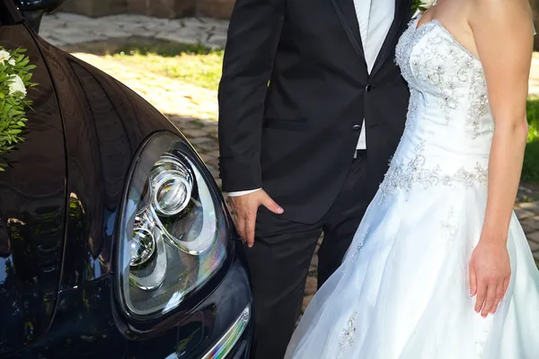 Joven novia y novio de pie cerca de un coche nuevo — Foto de Stock