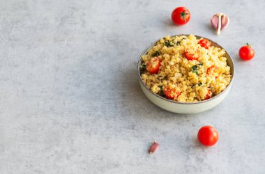 Domates, ıspanak ve sarımsaklı sağlıklı kinoa tarifi. Yatay, gri arkaplanda kopyalama alanı ile.