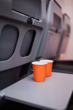 Orange disposable paper cups on the table in the plane during the flight.