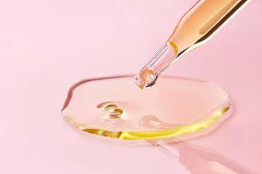 Pembe arka plana sıvı yağ dökerek pipeti kapat. Düşen bir damla aromaterapi yağı ile yakın plan.