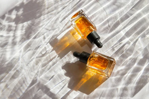 Çivi ve tırnak bakımı için şeffaf yağ cam şişelerde, beyaz arka planda doğal gölgeli pipet makinesi ile. Güzellik ve bakım konsepti. 