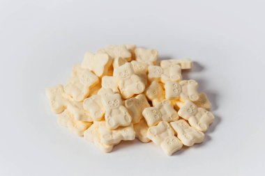 Açık sarı ayı, beyaz arka plana saçılmış çocukların vitaminlerini şekillendirdi. Çocuklar için vitaminler, çocuk hapları, haplar