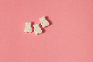 Pembe arka planda, fotokopi alanı olan beyaz oyuncak ayı vitaminleri. Çocuk hapları, hayvan şeklinde tabletler.