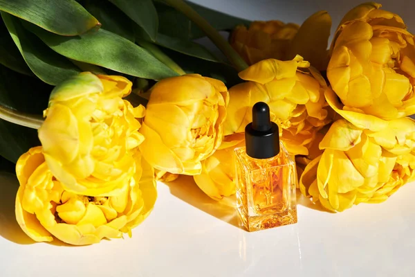 Transparent oil for nail and cuticle care in glass bottle with bunch of beautiful yellow Double Peony Tulip on a white background