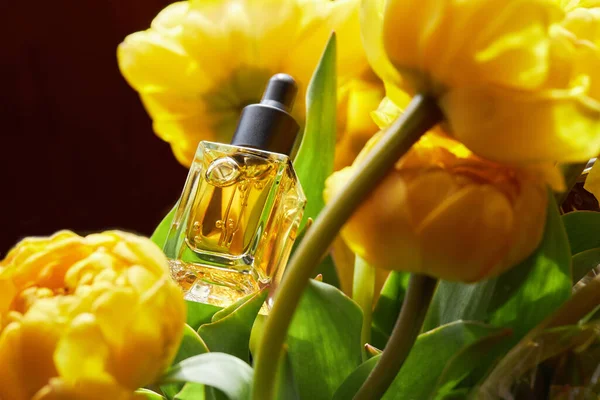 Transparent oil for nail and cuticle care in glass bottle with bunch of beautiful yellow Double Peony Tulip on a white background