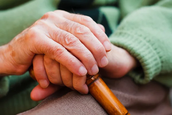 En äldre man sitter, vila händerna på en trä käpp. — Stockfoto