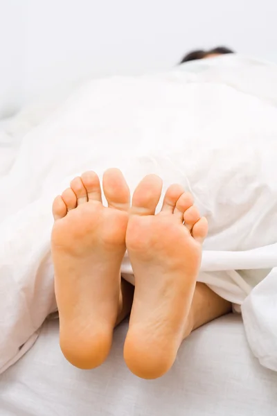 Una donna che dorme sotto il piumone con le gambe scoperte . — Foto Stock