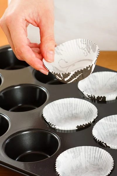 A female cook 's hand putting muffin cups in the oven pan. — Stock Photo, Image