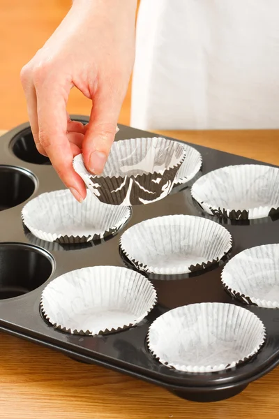 A female cook 's hand putting muffin cups in the oven pan. — Stock Photo, Image