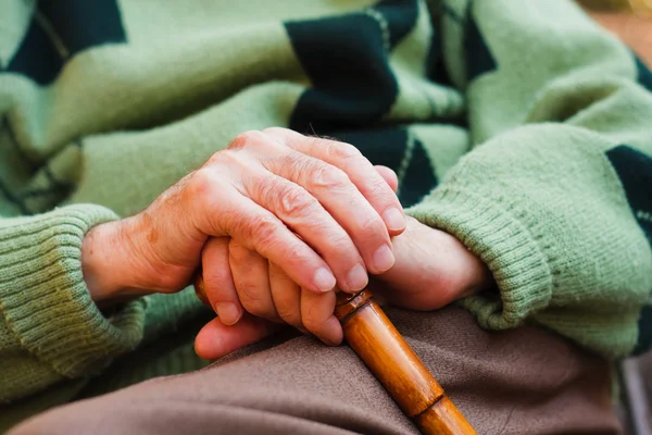 Een oudere man zitten, zijn handen rustend op een houten wandelstok. — Stockfoto