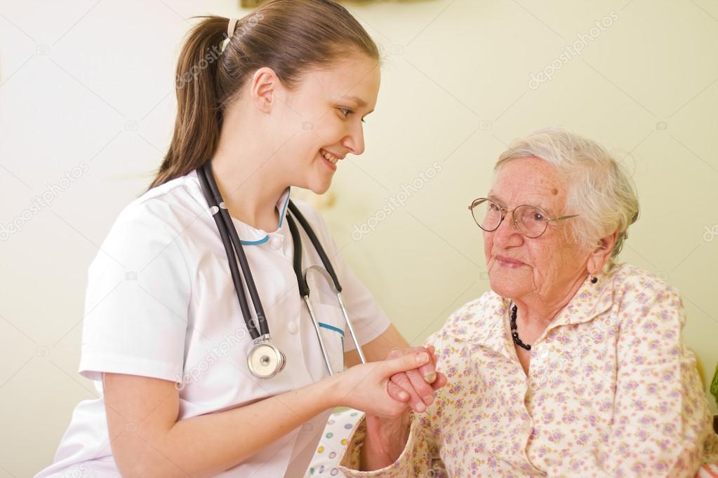 Nurse visiting an elderly sick woman socialising - talking - with her, holding her hands.