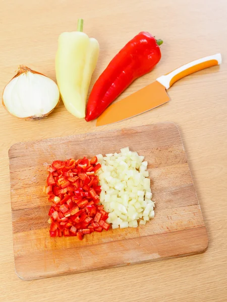 Peaces of paprika, whole pepper and half cut onion next to a knife. — Stock Photo, Image