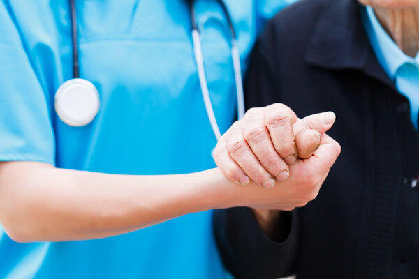 Заботливая медсестра держит пожилые руки
