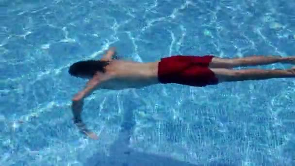 En man simmar under vattnet i en pool, kameran är under vatten — Stockvideo