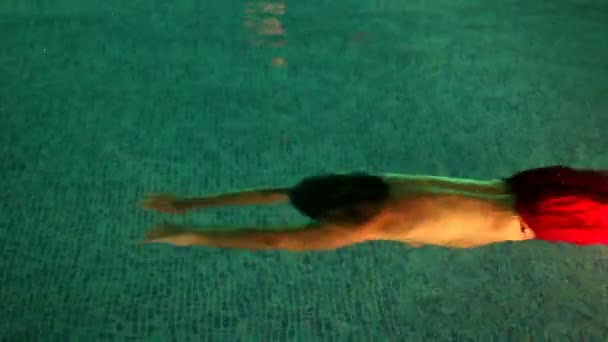 Un hombre está nadando bajo el agua en una piscina por la noche, la cámara está bajo el agua — Vídeos de Stock