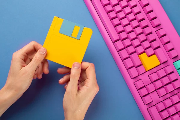 Hand holding floppy disk on color keyboard background, technology concept. High quality photo