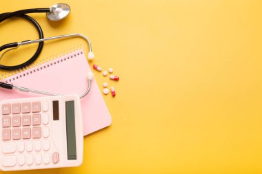 Pink beautiful calculator, notepad, stethoscope and vitamins or pills on a yellow background with a place for an inscription. High quality photo