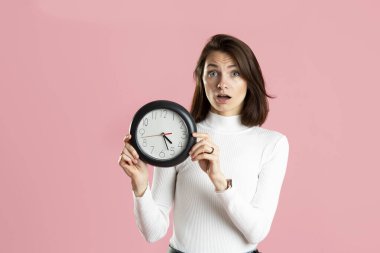 Young woman holding a clock on a pink background. High quality photo