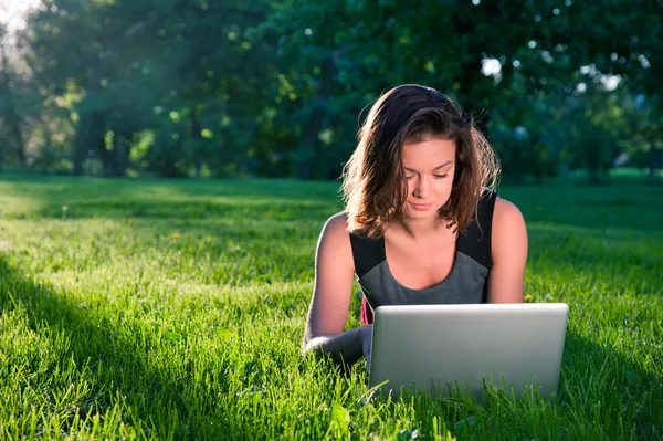 Mujer se sienta en la hierba con el ordenador portátil —  Fotos de Stock