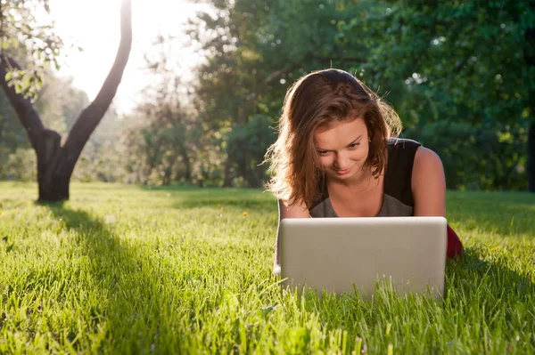 Mujer se sienta en la hierba con el ordenador portátil —  Fotos de Stock