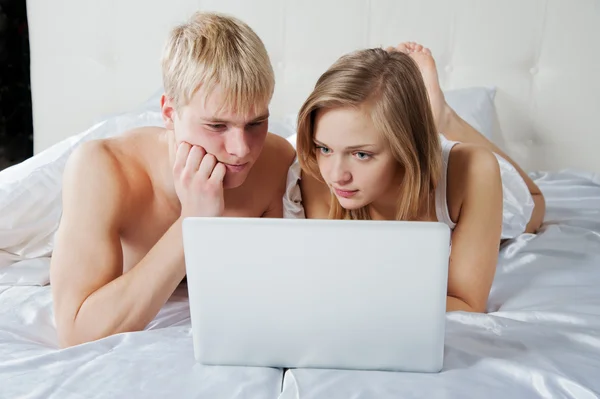 Chica y niño acostado en la cama con el ordenador portátil — Foto de Stock