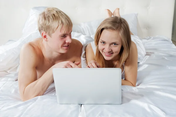 Girl and boy lying in bed with laptop — Stock Photo, Image