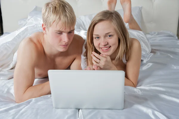 Chica y niño acostado en la cama con el ordenador portátil — Foto de Stock