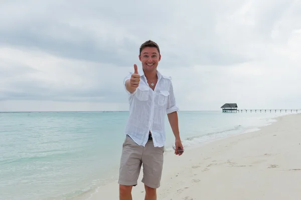 Man visar tummen på stranden nära havet — Stockfoto